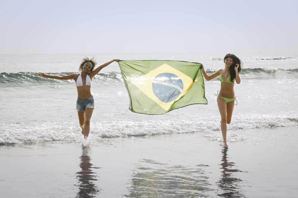 Young attractive girls on beach running with Brazil flag