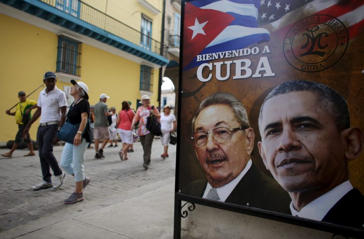 Tourists pass by images of U.S. President Barack Obama and Cuban President Raul Castro in a banner that reads "Welcome to Cuba" at the entrance of a restaurant in downtown Havana